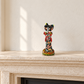 Colorful hand-painted ceramic mini Catrina figurine displayed on a cream stone fireplace mantel.