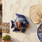 Blue Talavera-style ceramic fish wall décor displayed on a stucco wall in a coastal-inspired outdoor space.