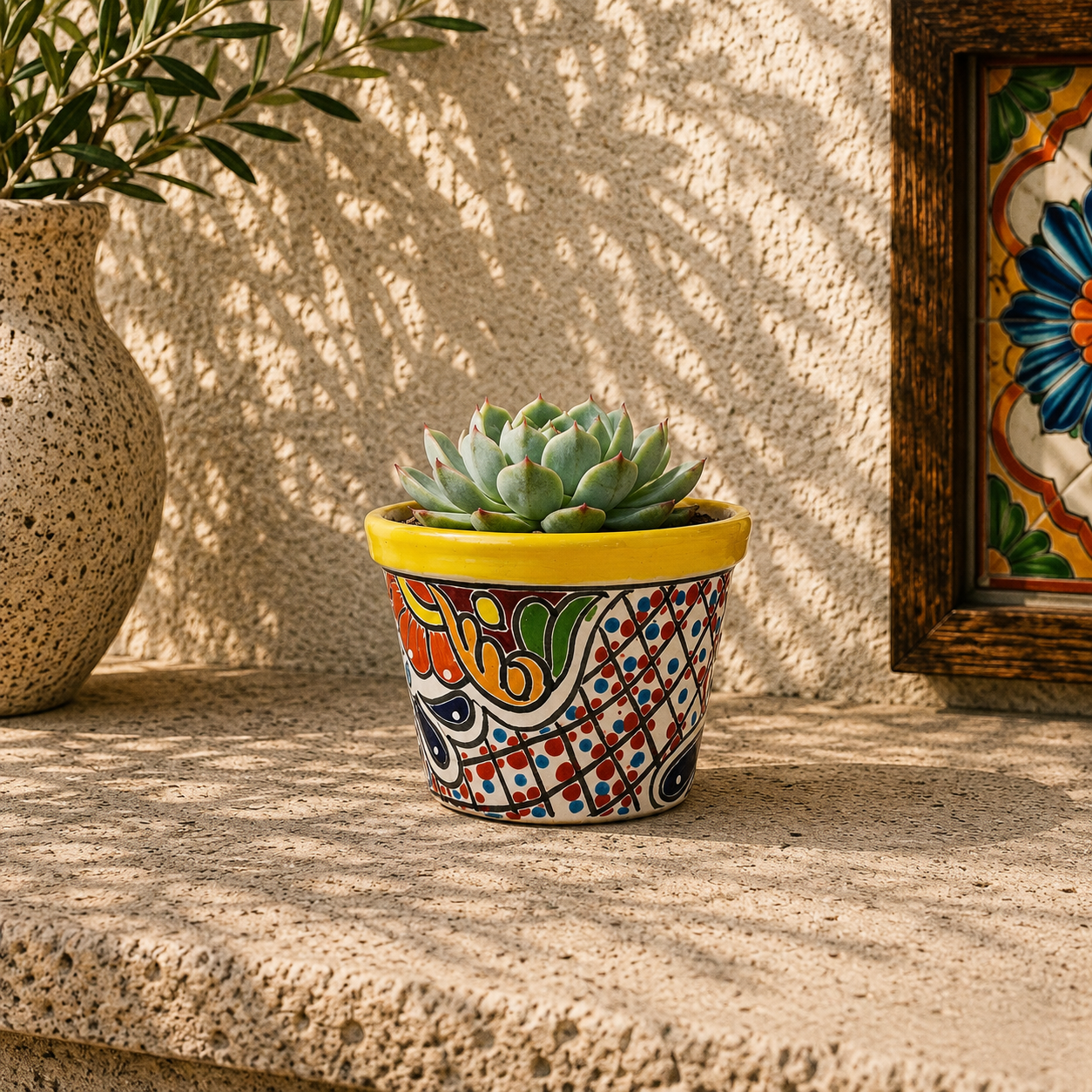 Yellow rim patterned ceramic planter holding a succulent on a textured stone surface beside a leafy plant and framed decorative tile artwork.
