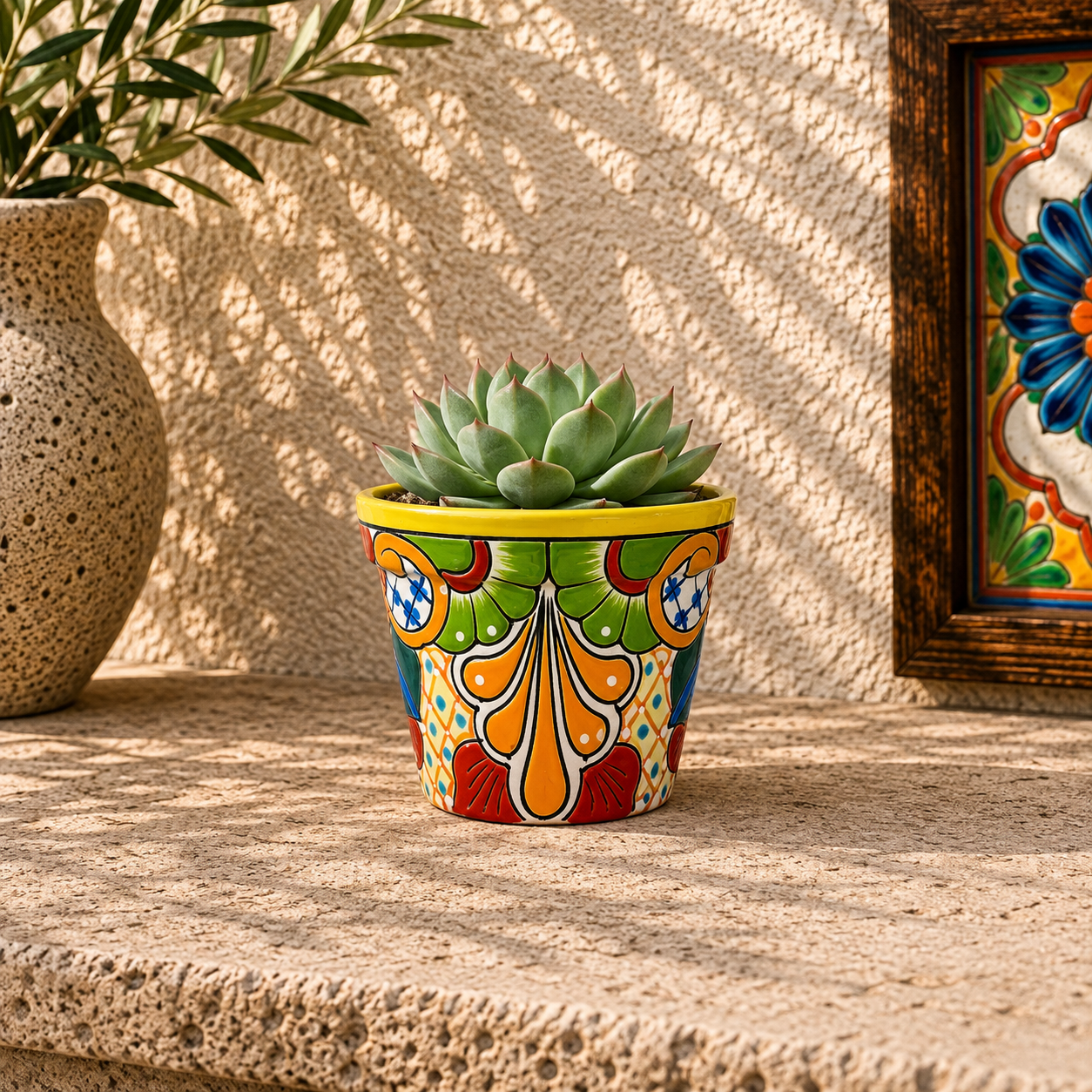 Yellow rim ceramic planter with green and orange artwork holding a succulent on a stone surface beside pottery and framed decorative tiles.

