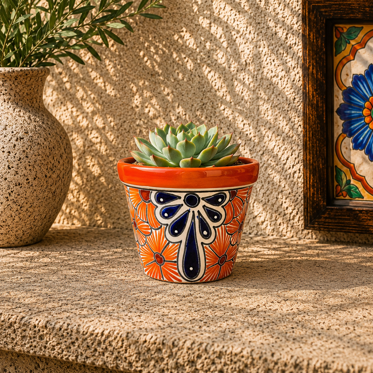 Red orange rim ceramic planter holding a succulent on a stone surface beside a speckled vase with leafy branches and framed floral tile artwork.

