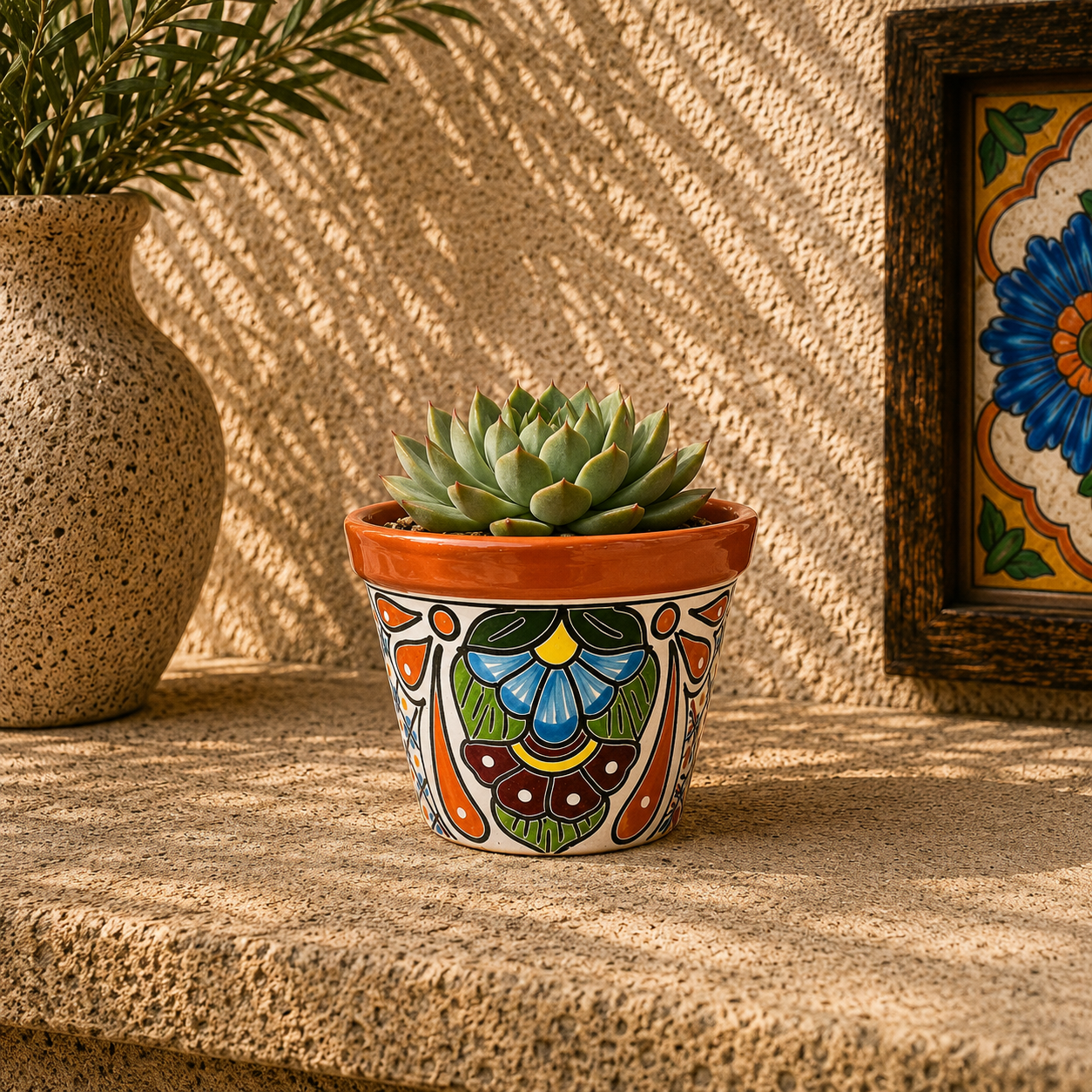 Red orange rim ceramic planter holding a succulent on a stone surface beside a speckled vase with leafy branches and framed floral tile artwork.
