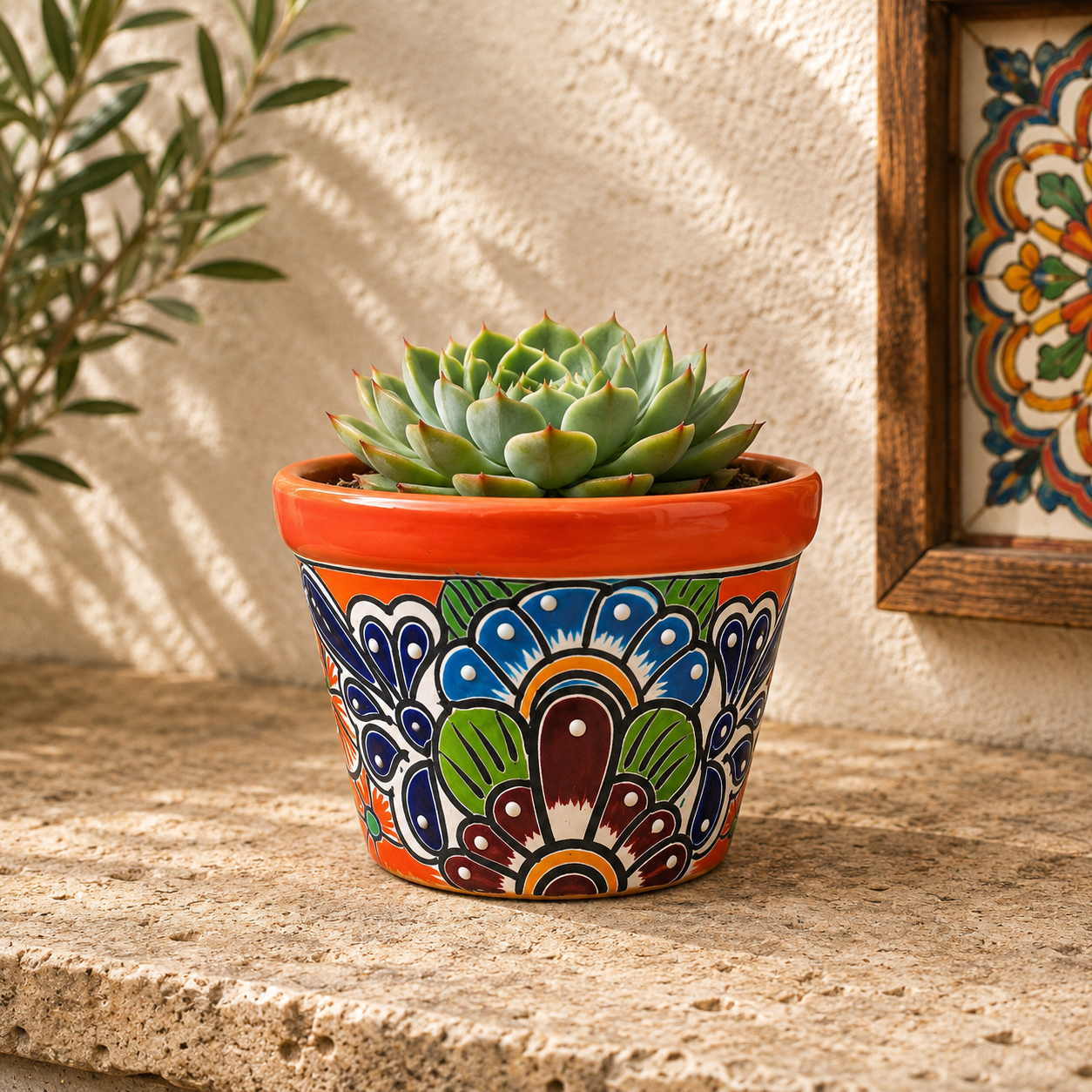 Red orange rim floral ceramic planter holding a succulent on a textured stone surface beside framed decorative tile artwork.
