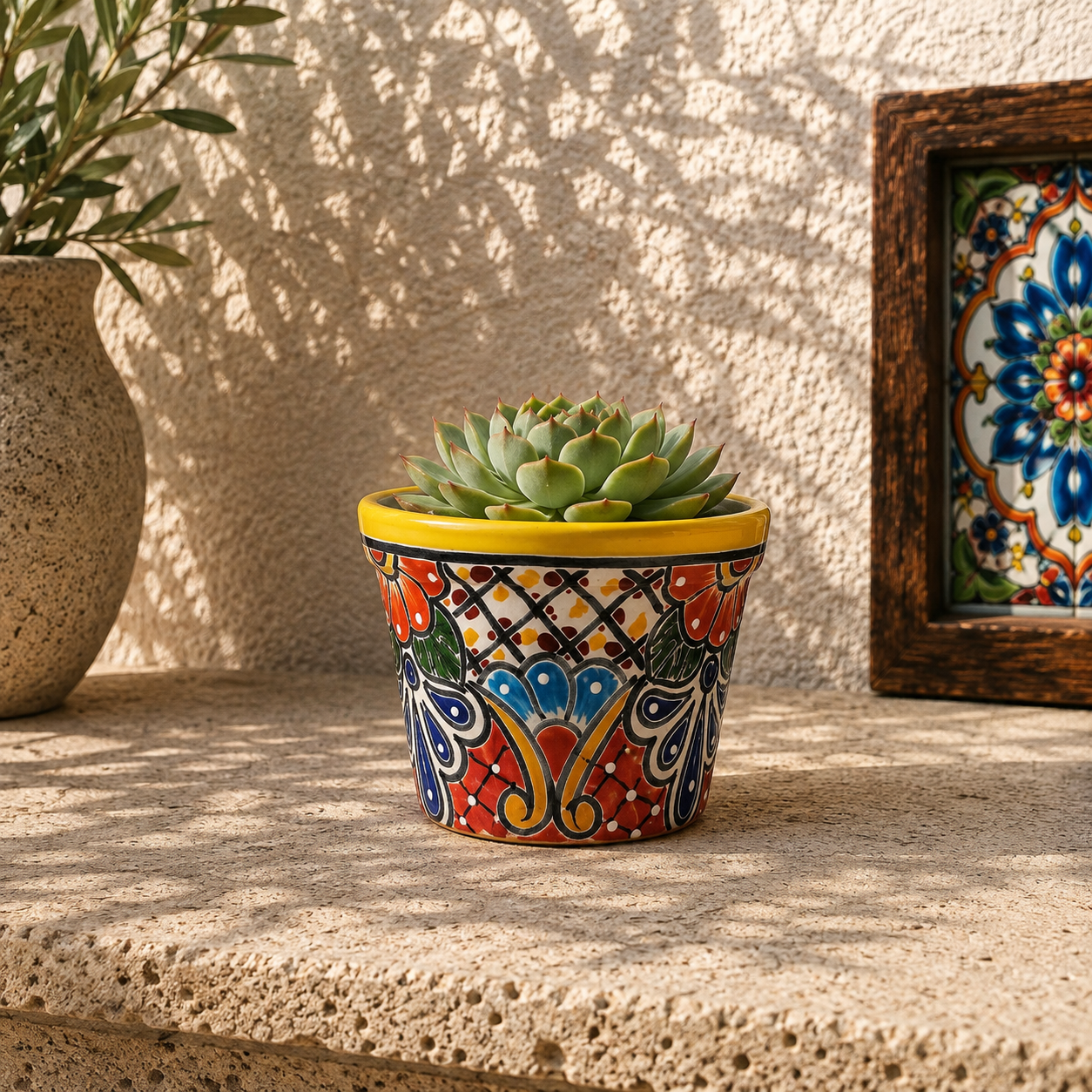 Yellow rim floral ceramic planter holding a succulent on a textured stone surface beside neutral pottery and framed decorative tile artwork.
