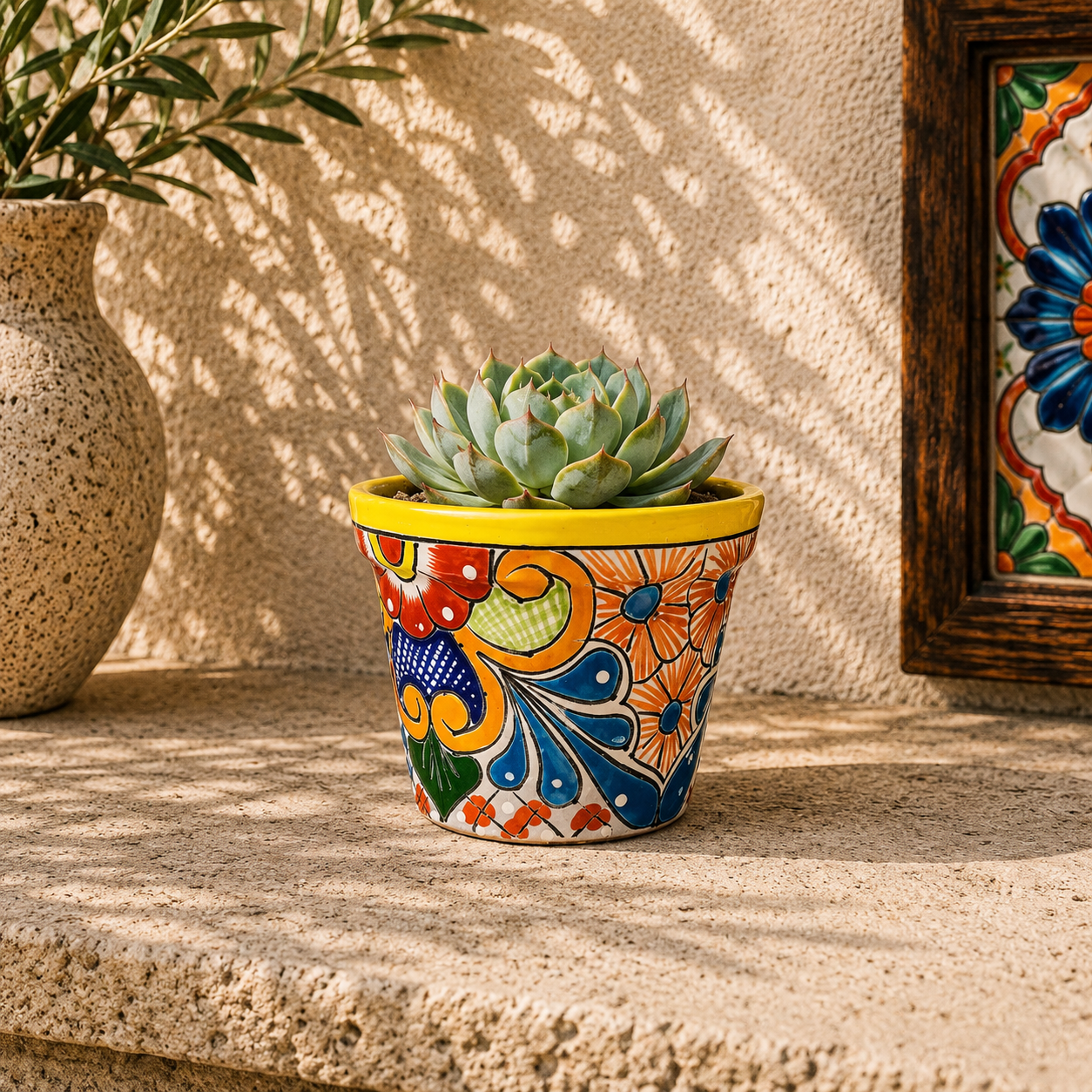Yellow rim ceramic planter with orange and blue floral artwork holding a succulent on a stone surface beside pottery and framed decorative tiles.
