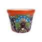 Red orange rim ceramic planter with sky blue and burgundy flowers, deep blue petals, green leaves, and white dotted highlights.

