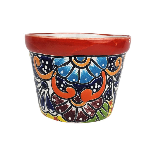 Red rim ceramic planter with sky blue and burgundy flowers, orange scrollwork, deep blue accents, and green leaves on a white background.

