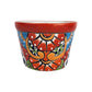 Red rim ceramic planter with red and orange flowers, golden-orange scrollwork, blue accents, and green lattice details on a white background.